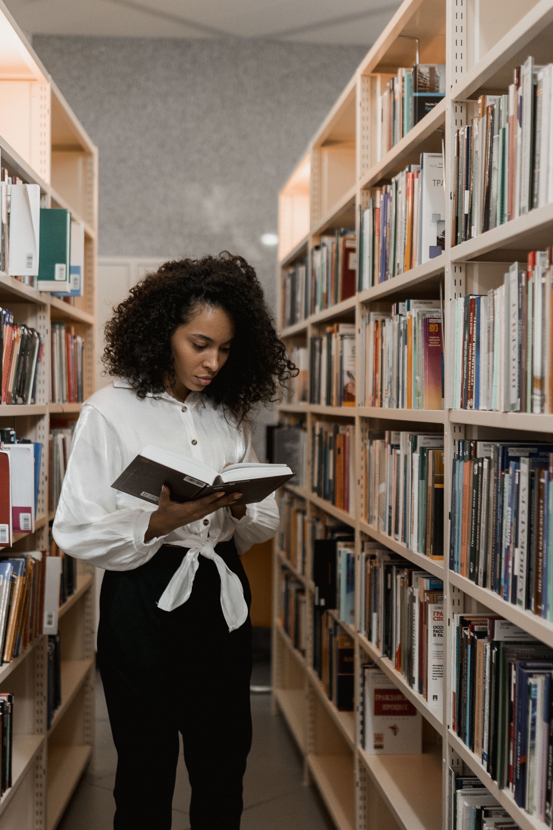 A young woman reading between tall library bookshelves