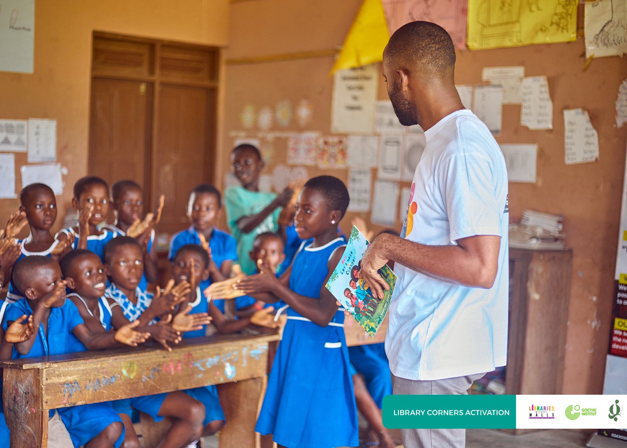 A volunteer handing out books to excited pupils in a classroom