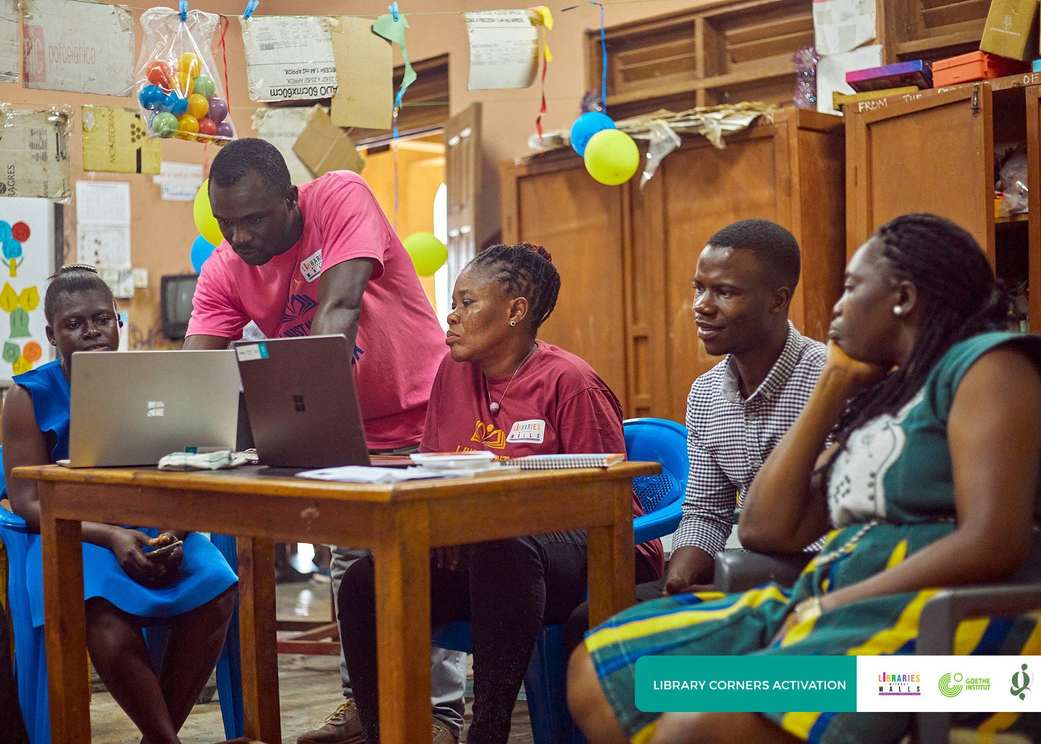 A facilitator guiding participants on laptops during a training session in a school