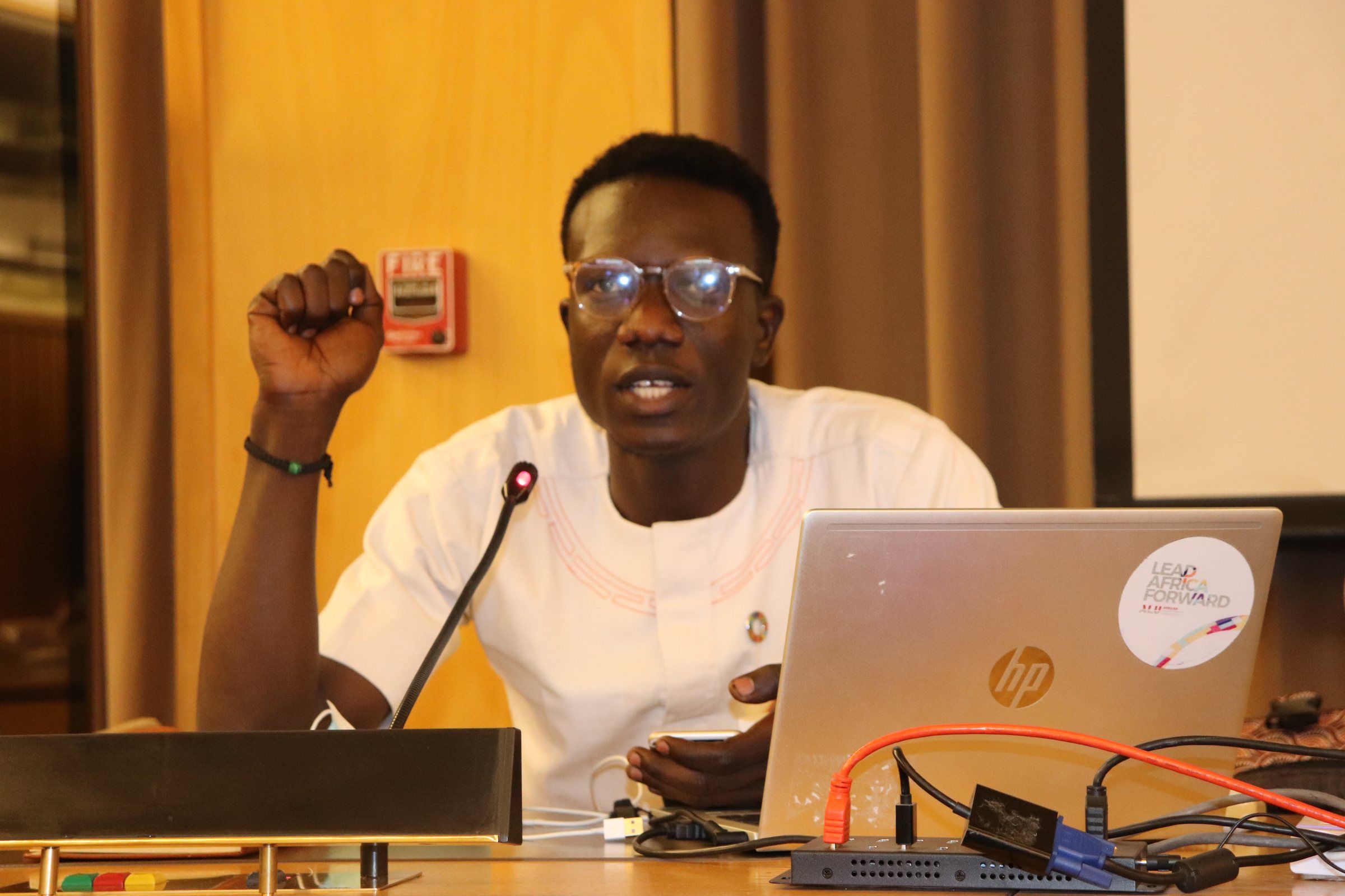 A young man speaking into a microphone at a workshop, a laptop open in front of him