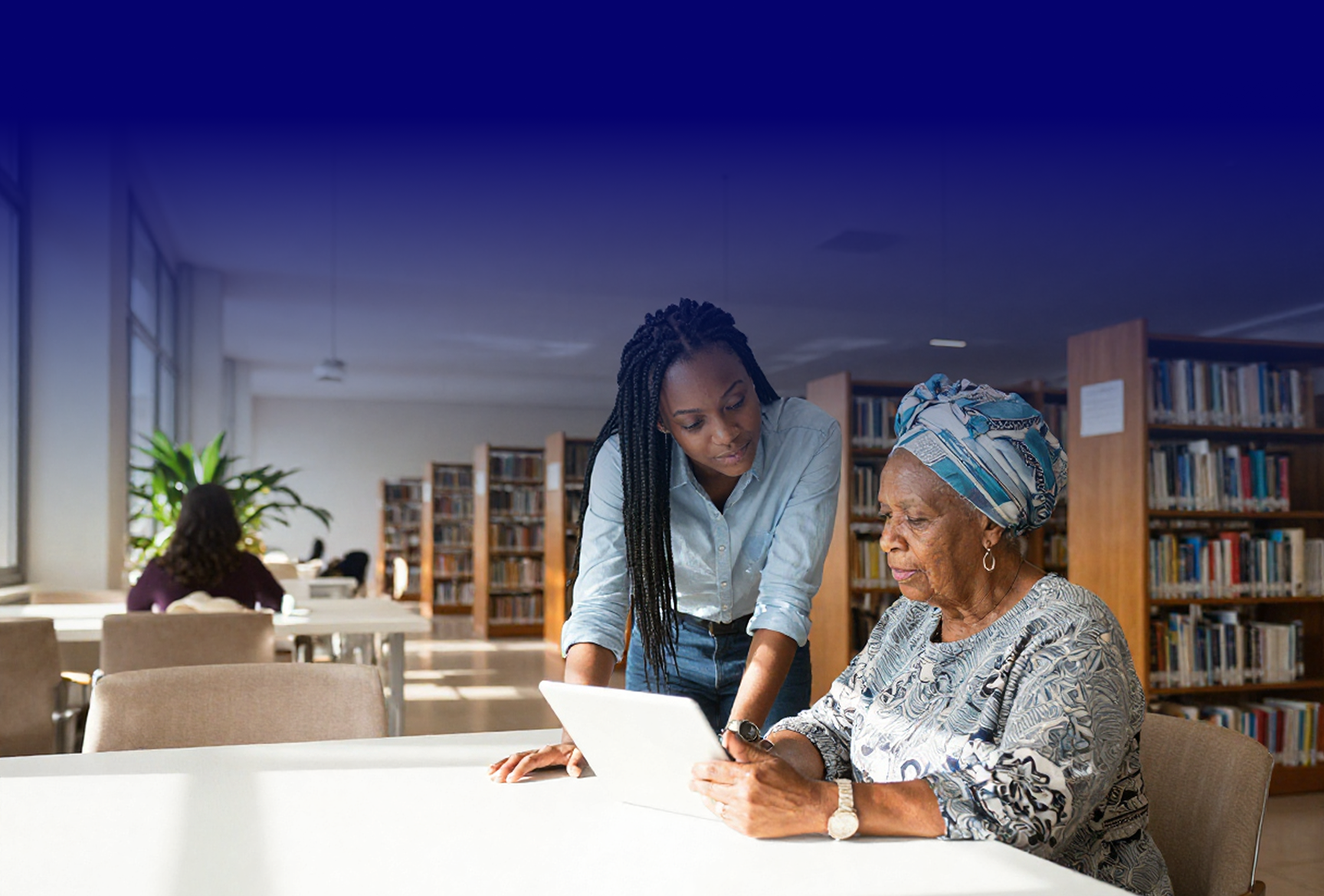 A young woman helping an older woman use a tablet in a library